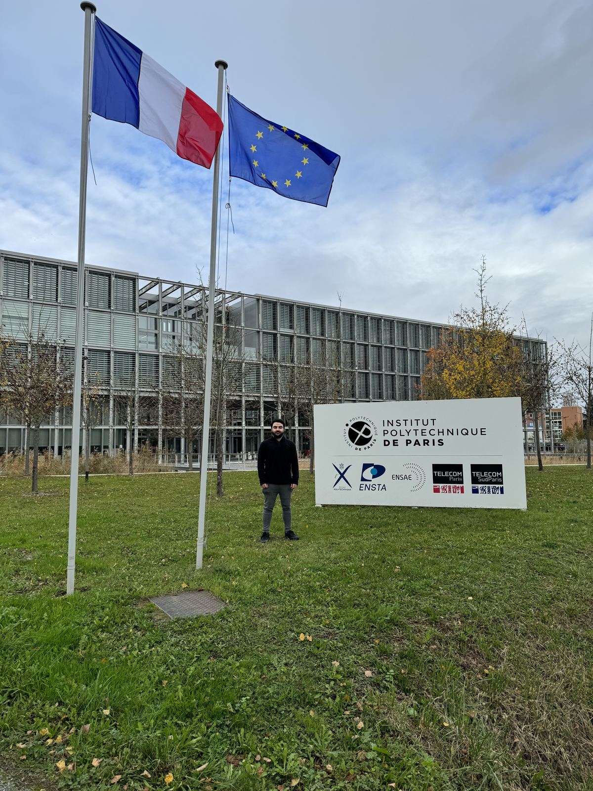 Peter Farah standing beside the Institut Polytechnique de Paris sign, French and EU flags flying overhead