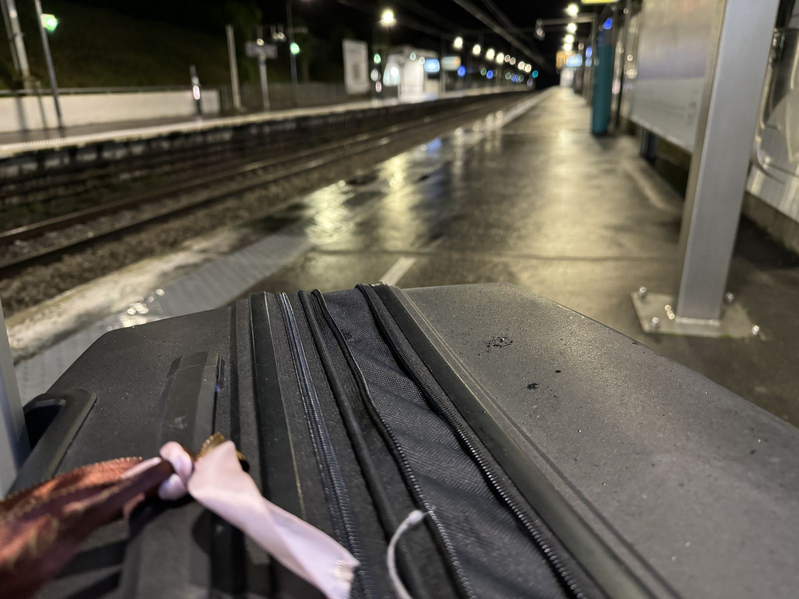 A suitcase on an empty, rain-slicked railway platform at night
