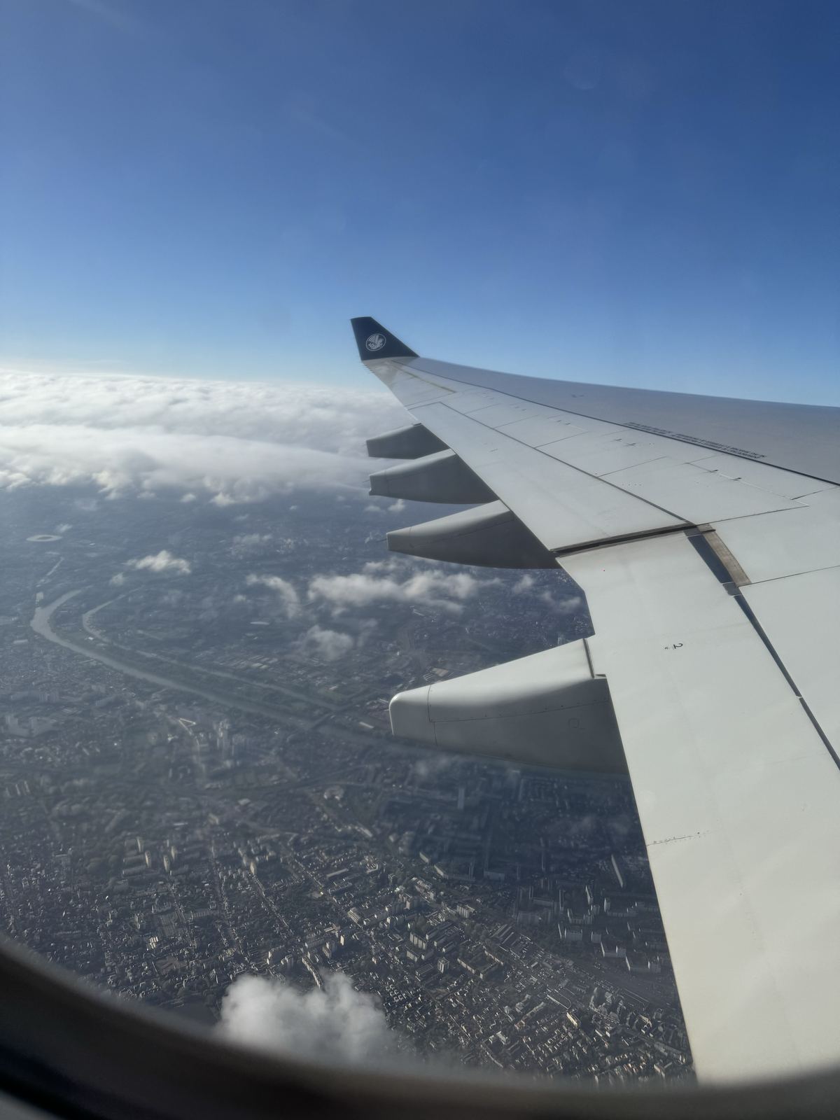 An aircraft wing above a city, seen through a cabin window