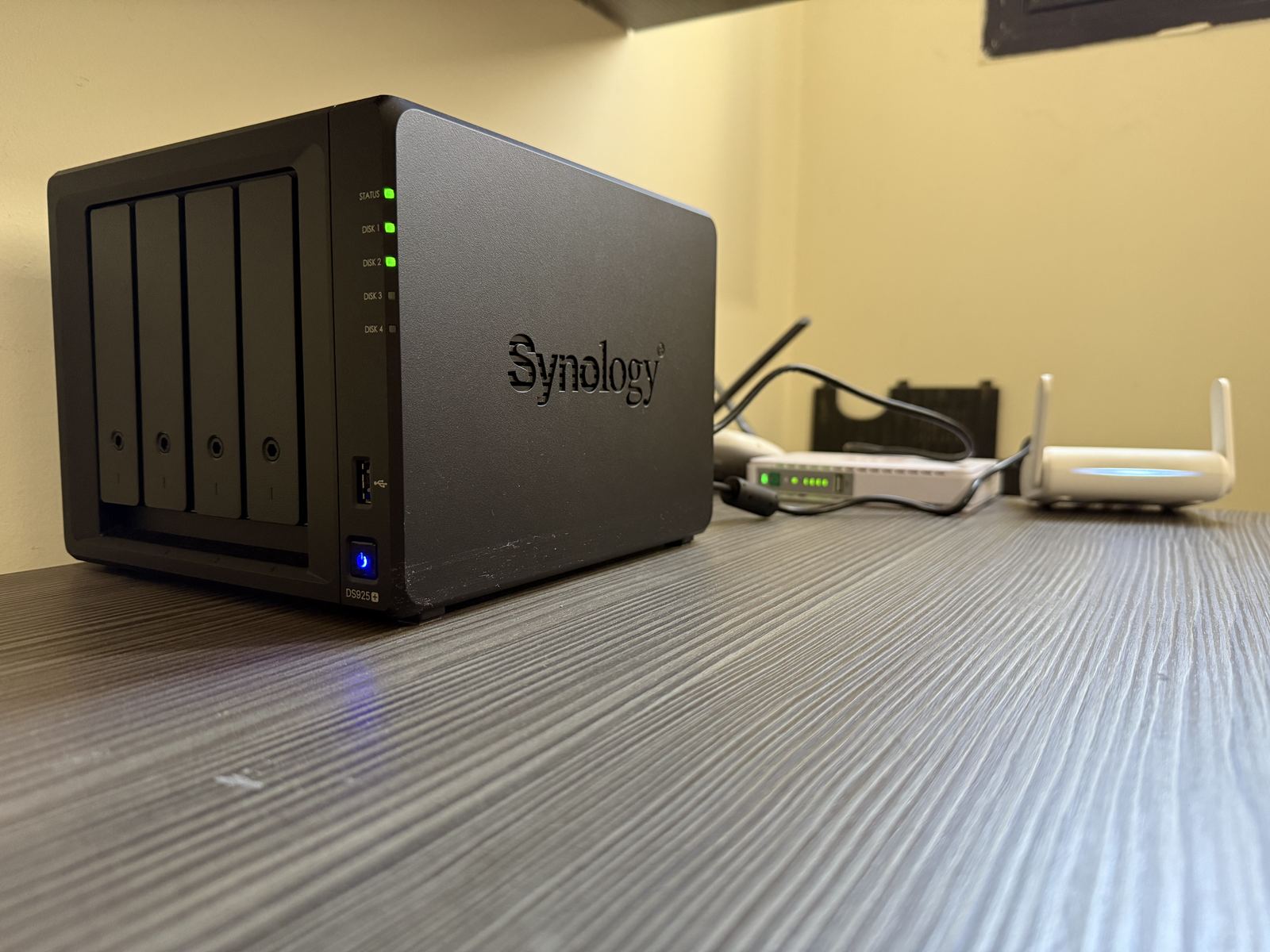 A four-bay Synology NAS beside a network switch and a wireless access point