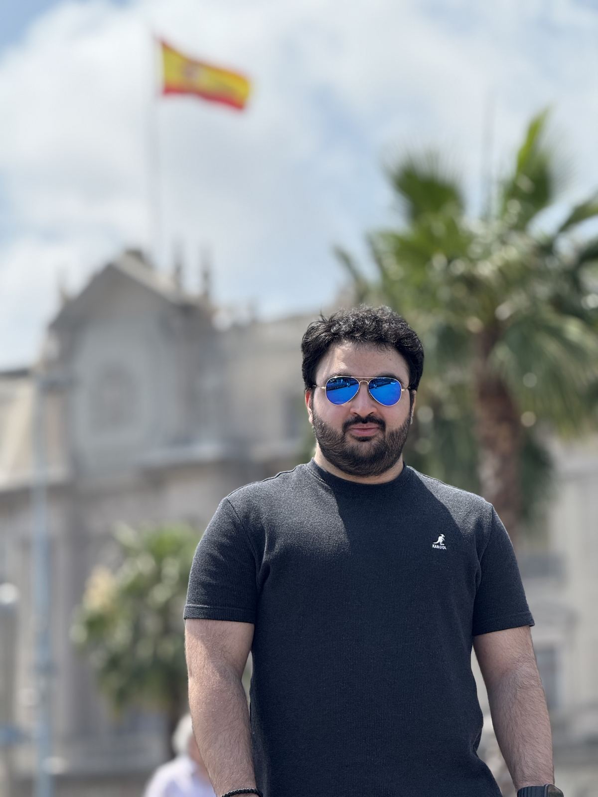 Peter Farah in sunglasses, a Spanish flag and a palm tree behind him